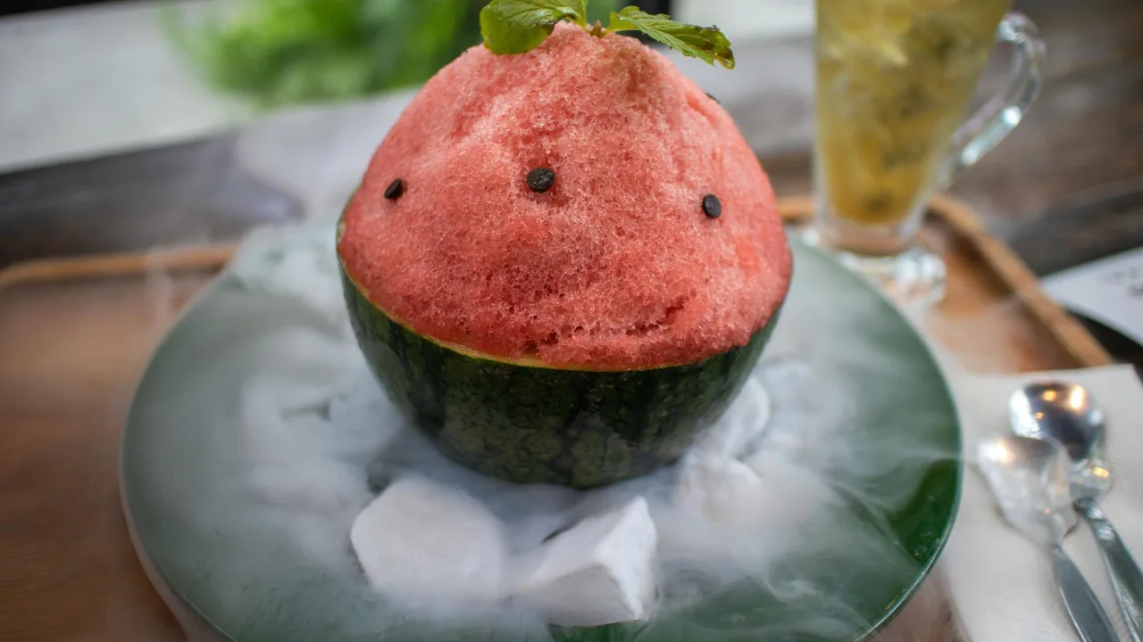 Close-up of a watermelon shaved ice dessert with mint garnish, paired with a refreshing drink.