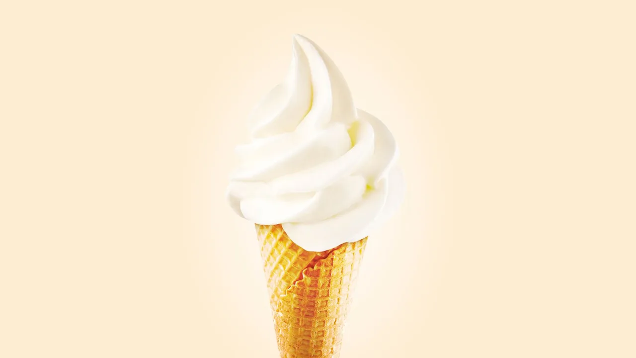 Close-up of a creamy soft serve ice cream cone on a bright background.