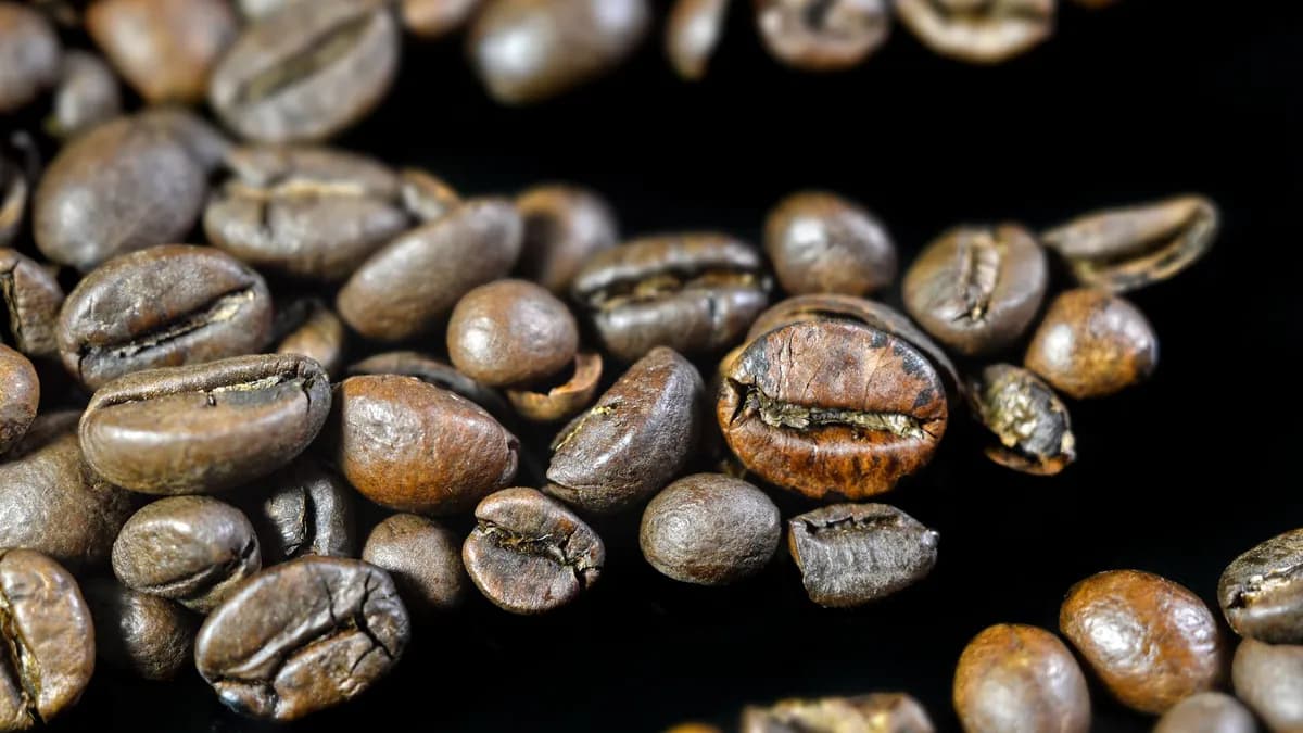 Detailed close-up image of aromatic roasted coffee beans scattered on a black surface.