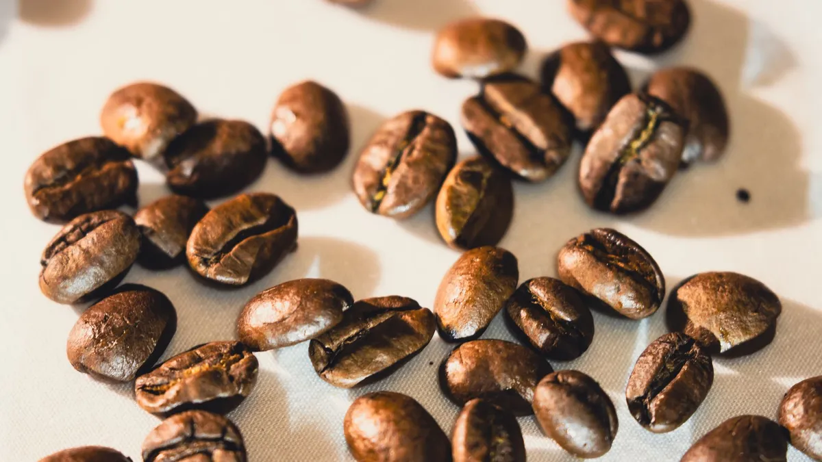 Bright close-up of roasted coffee beans scattered on white surface, ideal for coffee-themed designs.