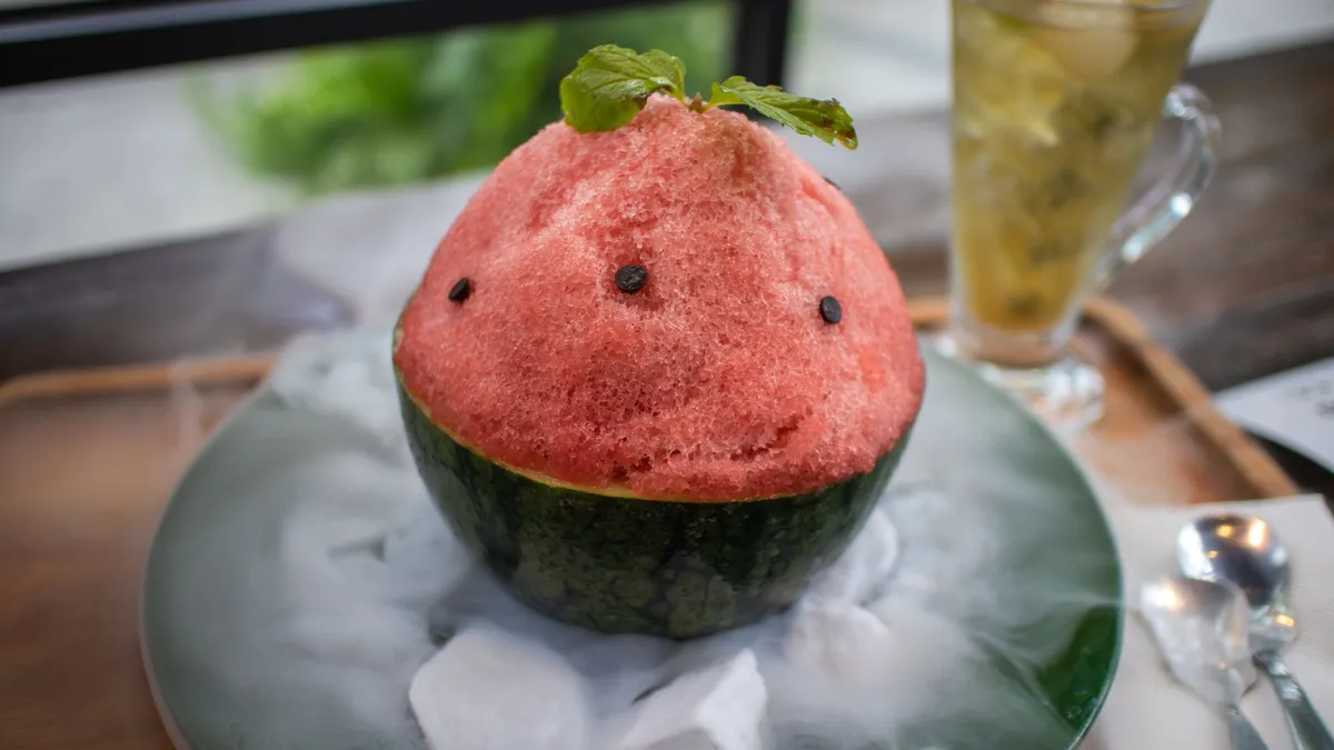 Close-up of a watermelon shaved ice dessert with mint garnish, paired with a refreshing drink.