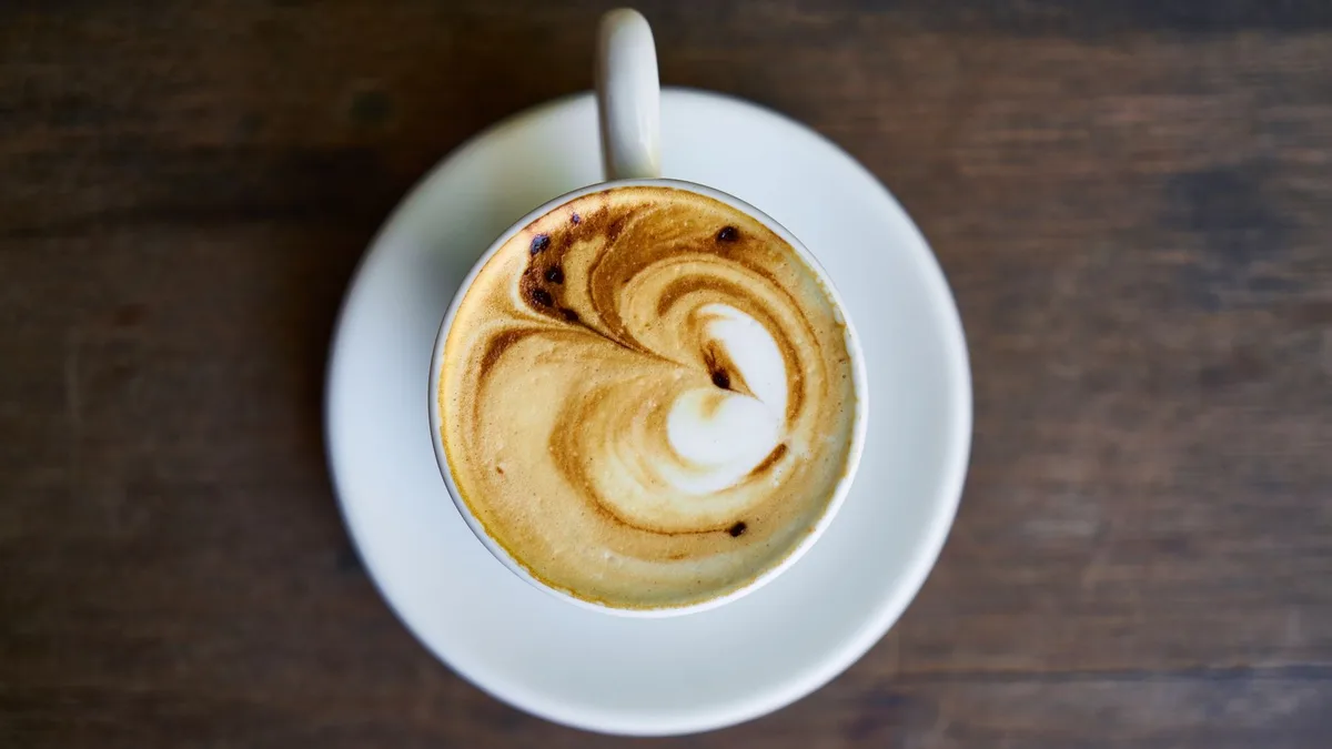 A ceramic cup of coffee with latte art, seen from above on a wooden table. Decorative stock image.